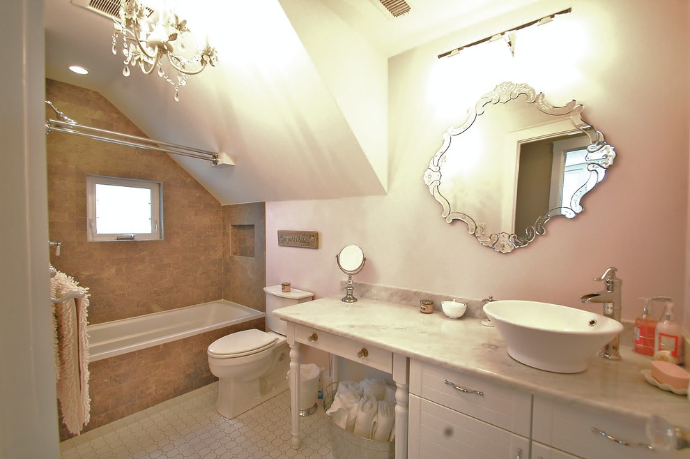 Inredning av ett modernt badrum, med ett fristående handfat, vita skåp, marmorbänkskiva, ett badkar i en alkov, en dusch/badkar-kombination, en toalettstol med separat cisternkåpa, beige kakel, stenkakel och släta luckor