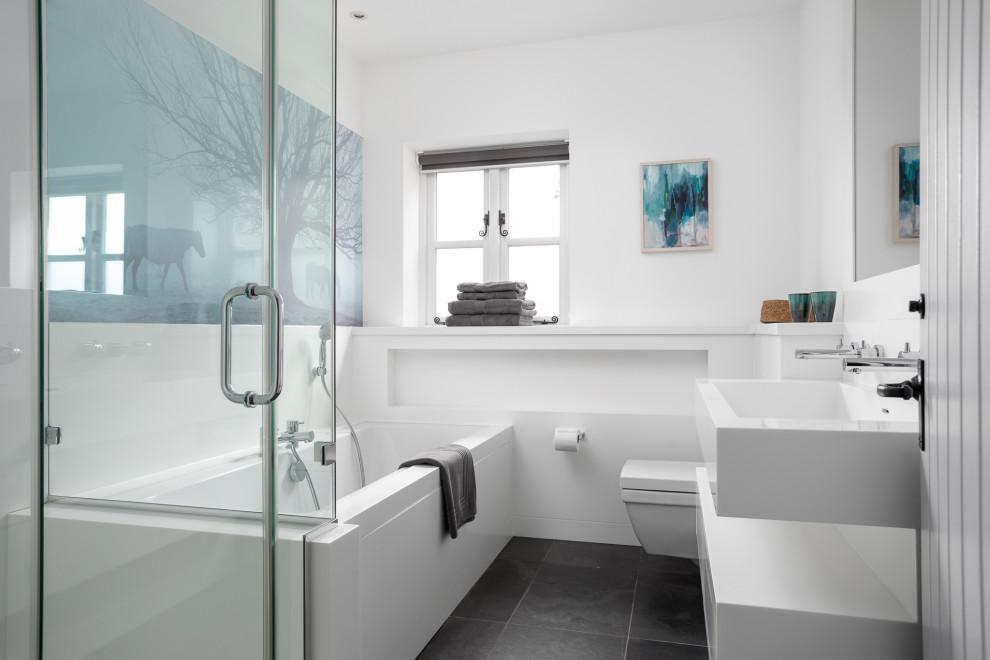 Exemple d'une salle de bain principale bord de mer de taille moyenne avec une baignoire d'angle, WC à poser, un mur blanc, un sol gris et un plan de toilette blanc.