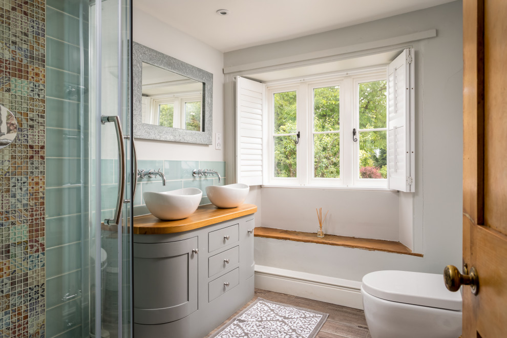 Photo of a medium sized rural shower room bathroom in Gloucestershire with grey cabinets, a one-piece toilet, a vessel sink, wooden worktops, brown worktops, shaker cabinets, green tiles, metro tiles, grey walls and brown floors.