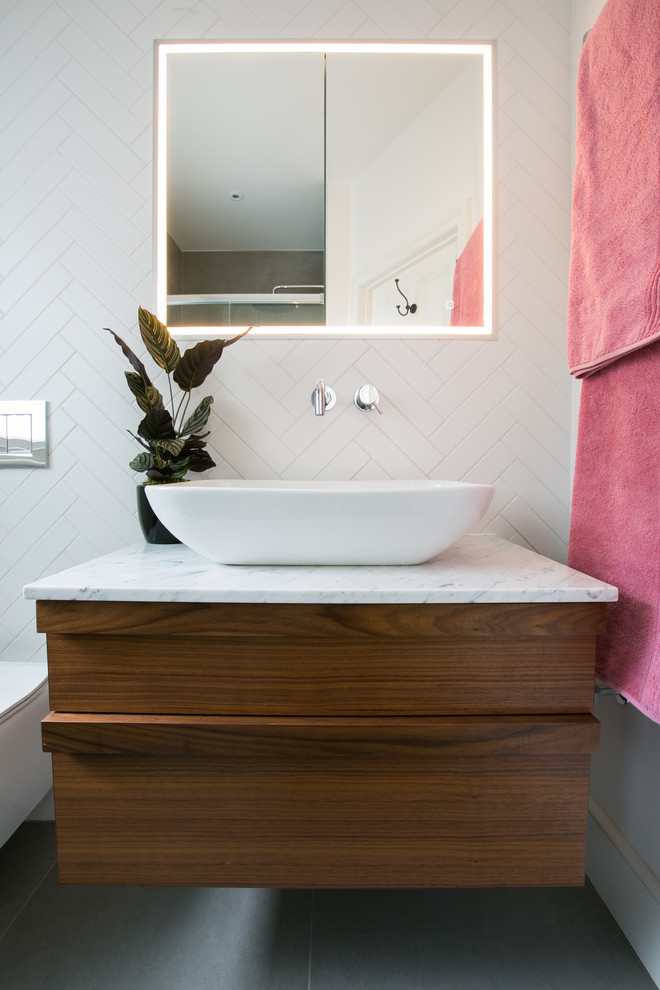 Photo of a medium sized contemporary bathroom in London with white cabinets, a corner bath, a shower/bath combination, a wall mounted toilet, white tiles, ceramic tiles, white walls, ceramic flooring, multi-coloured floors and an open shower.