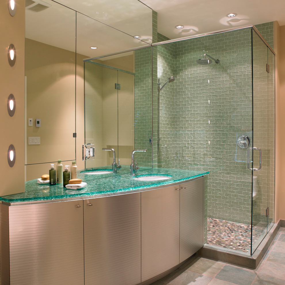 Modelo de cuarto de baño contemporáneo con armarios con paneles lisos, ducha esquinera, baldosas y/o azulejos verdes, baldosas y/o azulejos de vidrio, paredes beige, aseo y ducha, lavabo bajoencimera, encimera de vidrio, encimeras turquesas y espejo con luz