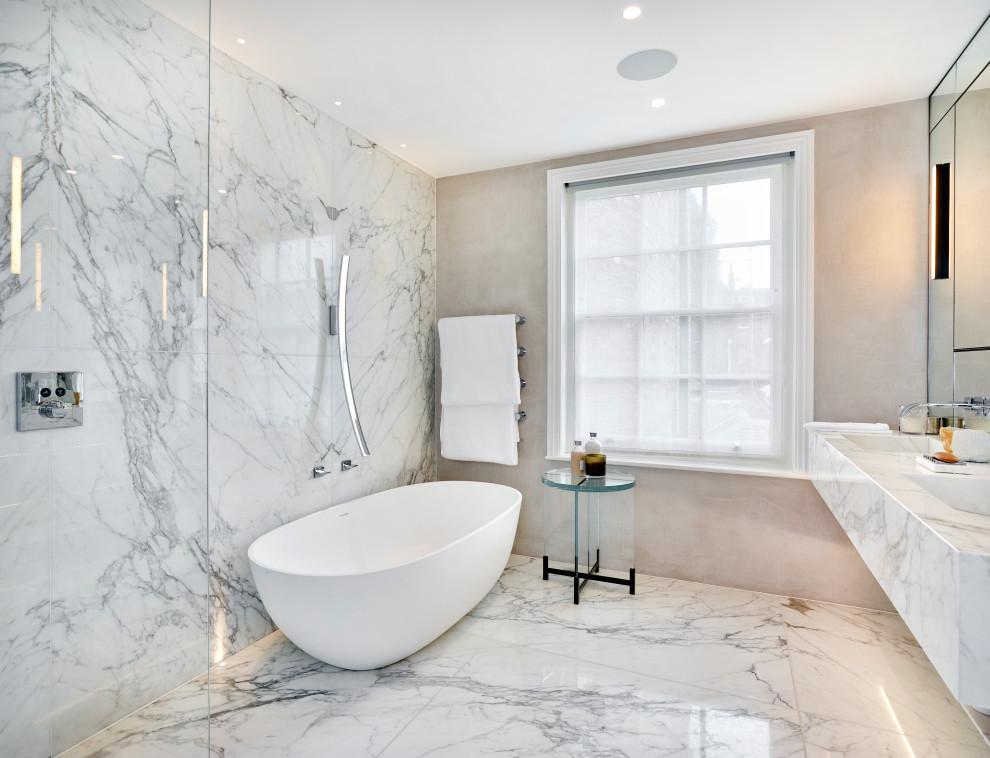 ロンドンにあるラグジュアリーな広いコンテンポラリースタイルのおしゃれなマスターバスルーム (大理石の洗面台、白いキャビネット、置き型浴槽、オープン型シャワー、グレーのタイル、ベージュの壁、一体型シンク、グレーの床、オープンシャワー、白い洗面カウンター) の写真