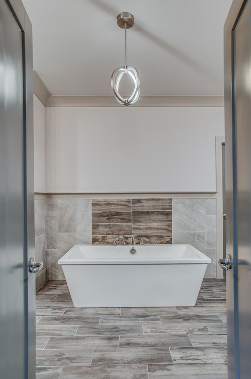 This is an example of a large traditional ensuite bathroom in Nashville with recessed-panel cabinets, blue cabinets, a freestanding bath, grey tiles, stone tiles, white walls, light hardwood flooring, a submerged sink, engineered stone worktops, grey floors, a walk-in shower and an open shower.