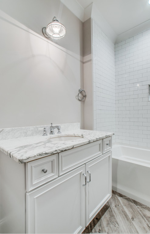 Photo of a medium sized classic shower room bathroom in Nashville with beaded cabinets, white cabinets, an alcove bath, a shower/bath combination, white tiles, metro tiles, grey walls, medium hardwood flooring, a submerged sink, marble worktops, brown floors and a shower curtain.