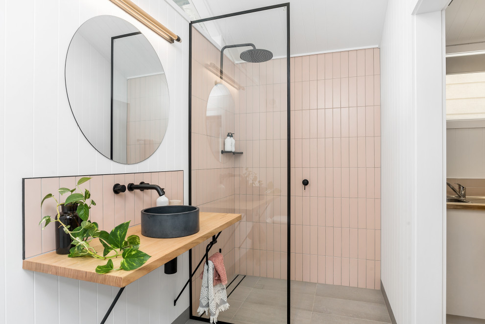 Modern inredning av ett mellanstort beige beige badrum med dusch, med en kantlös dusch, rosa kakel, ett fristående handfat, träbänkskiva, grått golv och med dusch som är öppen