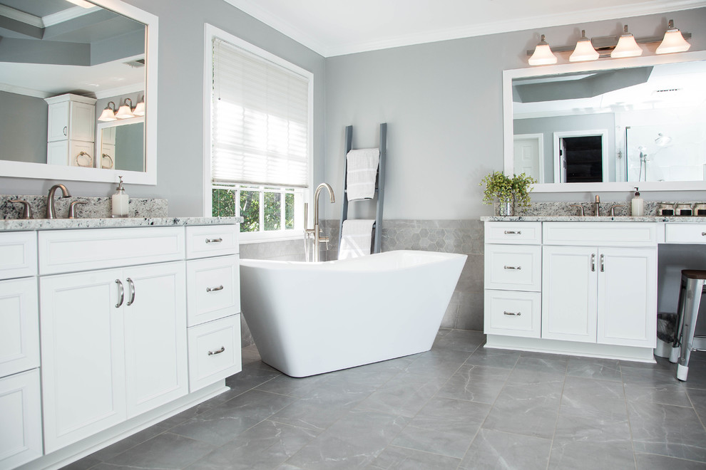 Inspiration for a large contemporary ensuite bathroom in Atlanta with shaker cabinets, white cabinets, a freestanding bath, a walk-in shower, a two-piece toilet, grey tiles, porcelain tiles, grey walls, ceramic flooring, a submerged sink, granite worktops, grey floors, a hinged door and white worktops.