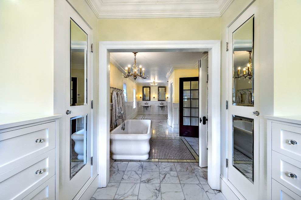 Exemple d'une grande douche en alcôve principale chic avec un placard avec porte à panneau encastré, des portes de placard blanches, une baignoire indépendante, un carrelage gris, un carrelage blanc, un carrelage de pierre, un mur jaune, un sol en marbre et un lavabo suspendu.