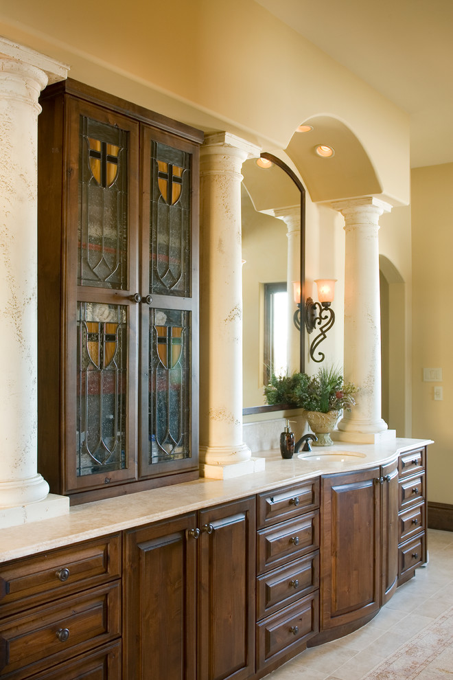 Immagine di un'ampia stanza da bagno padronale chic con ante con bugna sagomata, ante in legno scuro, pareti beige, pavimento in travertino, lavabo sottopiano e top in marmo