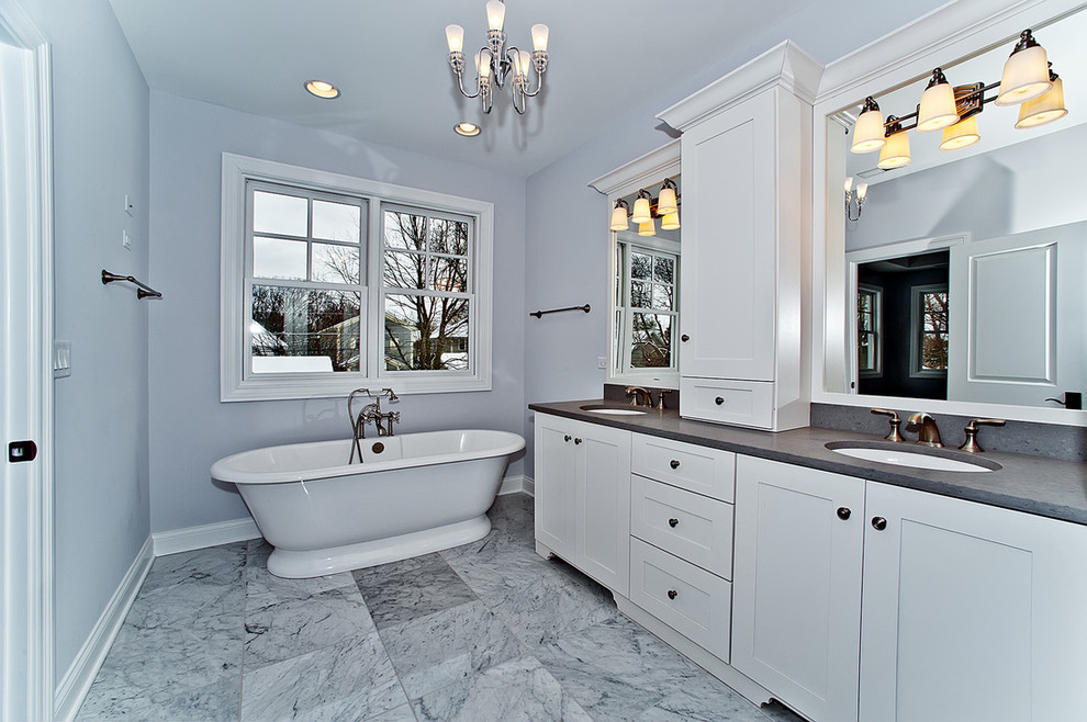 Cette image montre une salle de bain principale traditionnelle de taille moyenne avec un placard à porte shaker, des portes de placard blanches, une baignoire indépendante, un mur gris, un sol en marbre, un lavabo encastré, un plan de toilette en stéatite, un sol gris et un plan de toilette gris.