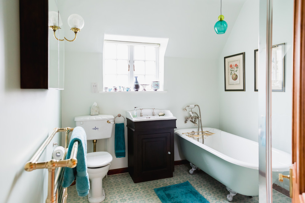 Elegant blue floor claw-foot bathtub photo in London with raised-panel cabinets, dark wood cabinets, a two-piece toilet, white walls and a console sink