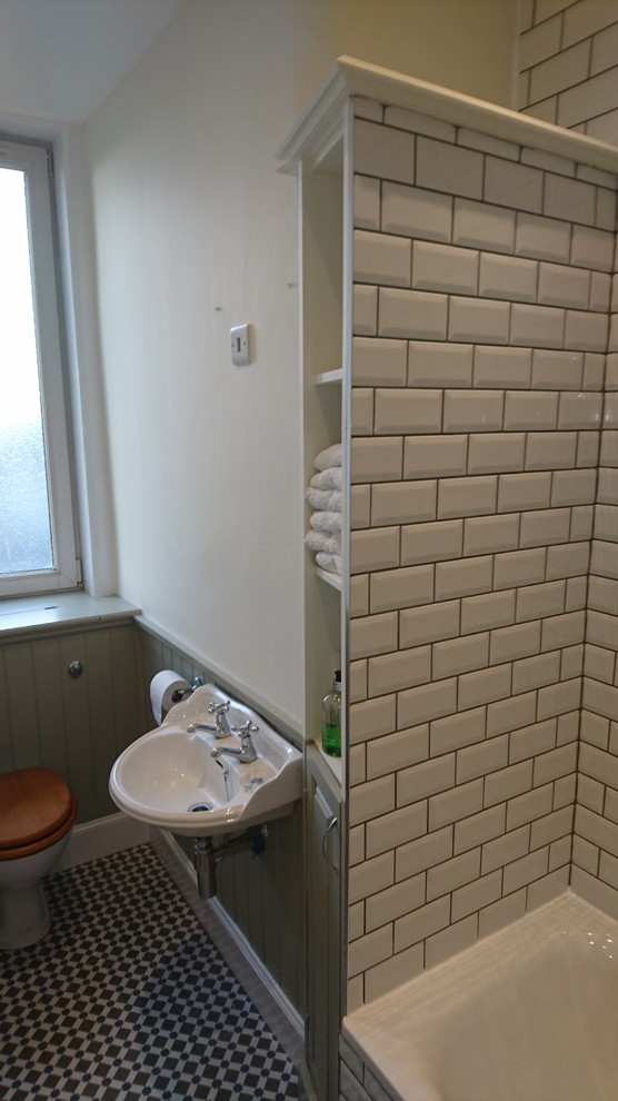 Klassisk inredning av ett litet badrum, med luckor med upphöjd panel, ett platsbyggt badkar, en dusch i en alkov, vit kakel, tunnelbanekakel, vita väggar och klinkergolv i keramik