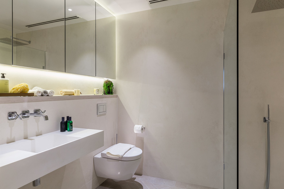 Modern inredning av ett litet en-suite badrum, med en vägghängd toalettstol, grå kakel, grå väggar, ett väggmonterat handfat, grått golv och med dusch som är öppen