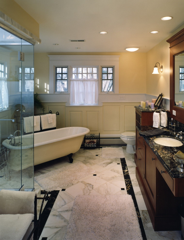 На фото: ванная комната в классическом стиле с ванной на ножках, угловым душем, разноцветной плиткой и желтыми стенами с