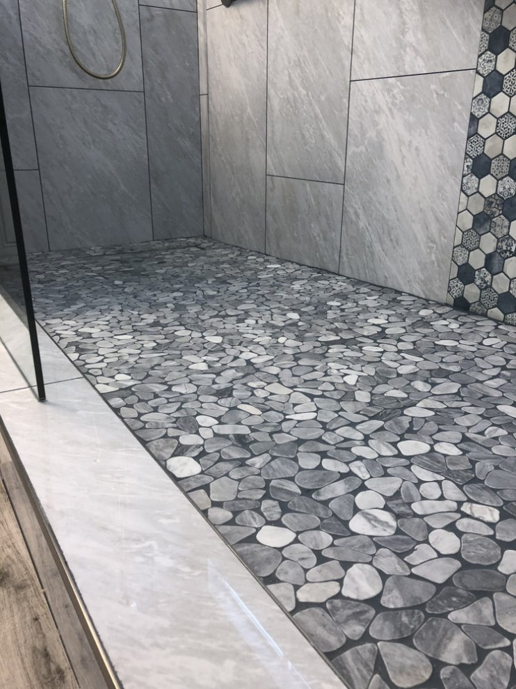 Inredning av ett badrum, med grå kakel, mosaik, klinkergolv i småsten, grått golv och grå väggar