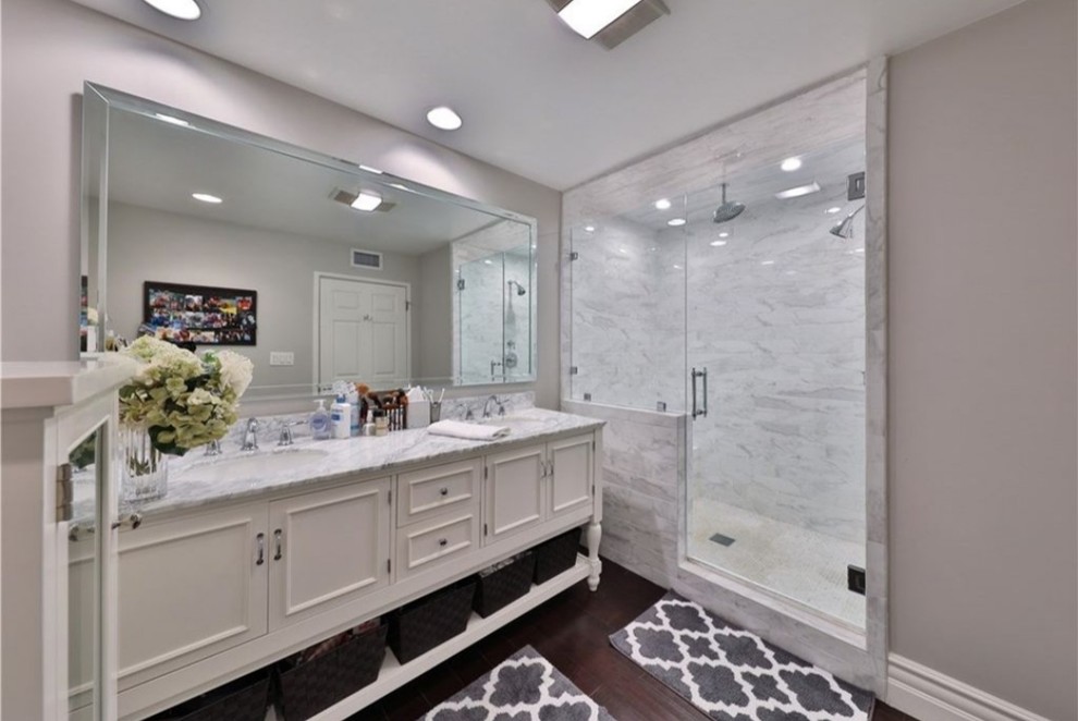 Medium sized classic ensuite bathroom in Orange County with beaded cabinets, white cabinets, an alcove shower, grey tiles, marble tiles, grey walls, dark hardwood flooring, a submerged sink, marble worktops, brown floors, a hinged door and grey worktops.