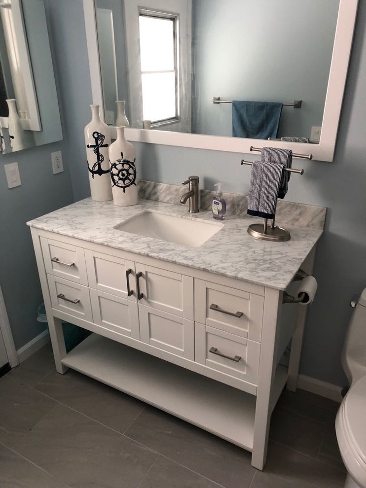 This is an example of a medium sized beach style bathroom in Los Angeles with shaker cabinets, white cabinets, blue walls, porcelain flooring, a submerged sink, marble worktops, grey floors and grey worktops.