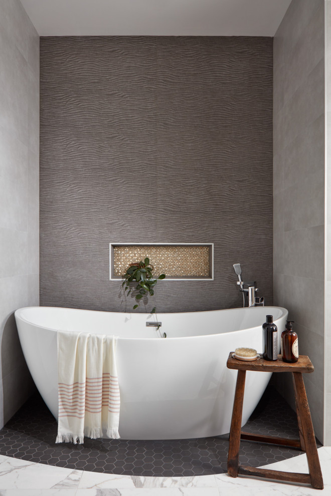 Modelo de cuarto de baño actual con bañera exenta, baldosas y/o azulejos grises, suelo con mosaicos de baldosas y suelo gris