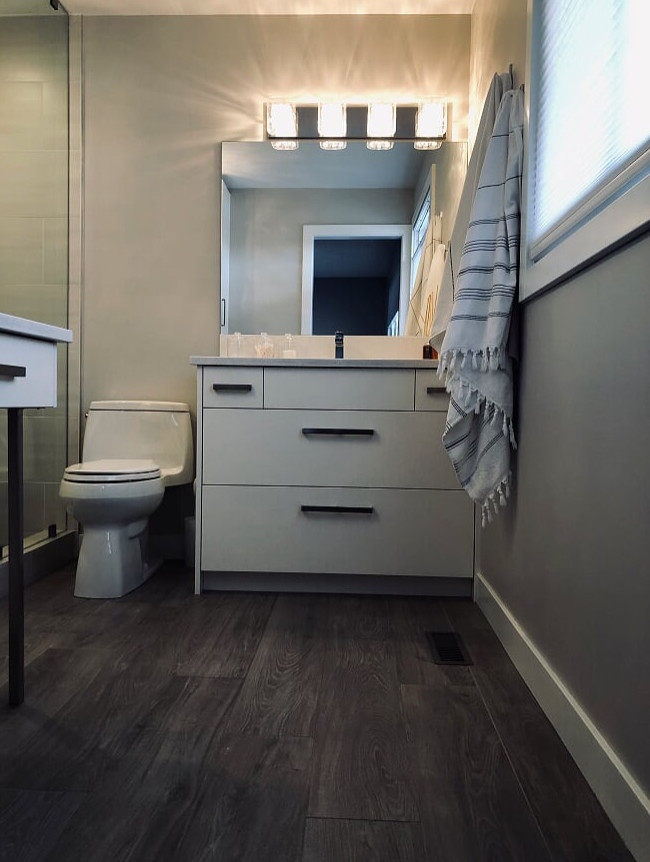 This is an example of a medium sized contemporary shower room bathroom in Calgary with a one-piece toilet, dark hardwood flooring, brown floors, flat-panel cabinets, white cabinets, white worktops, an alcove shower, grey tiles, porcelain tiles, grey walls, a submerged sink and a hinged door.