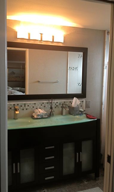 На фото: маленькая главная ванная комната в морском стиле с плоскими фасадами, темными деревянными фасадами, стеклянной столешницей, разноцветной плиткой, стеклянной плиткой, накладной ванной, душем над ванной, унитазом-моноблоком, монолитной раковиной, серыми стенами и полом из галечной плитки для на участке и в саду