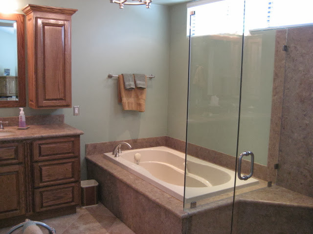 Medium sized classic ensuite bathroom in Orange County with a submerged sink, raised-panel cabinets, medium wood cabinets, solid surface worktops, a built-in bath, a corner shower, a two-piece toilet, beige tiles, ceramic tiles, green walls and travertine flooring.
