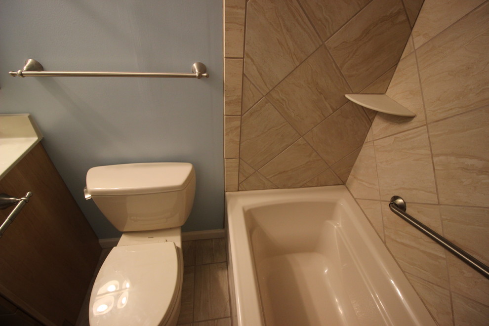 Cette image montre une petite salle d'eau marine en bois clair avec un placard avec porte à panneau encastré, un combiné douche/baignoire, WC séparés, un carrelage beige, un mur bleu, un sol en carrelage de céramique, un lavabo posé et un plan de toilette en marbre.
