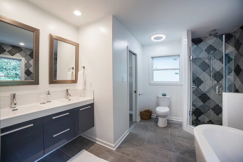 Inspiration pour une salle de bain principale minimaliste de taille moyenne avec un placard à porte plane, des portes de placard grises, une baignoire indépendante, une douche d'angle, WC séparés, un carrelage noir, un carrelage gris, des carreaux de porcelaine, un mur blanc, un sol en carrelage de porcelaine, un lavabo intégré, un plan de toilette en surface solide, un sol gris, une cabine de douche à porte battante et un plan de toilette blanc.