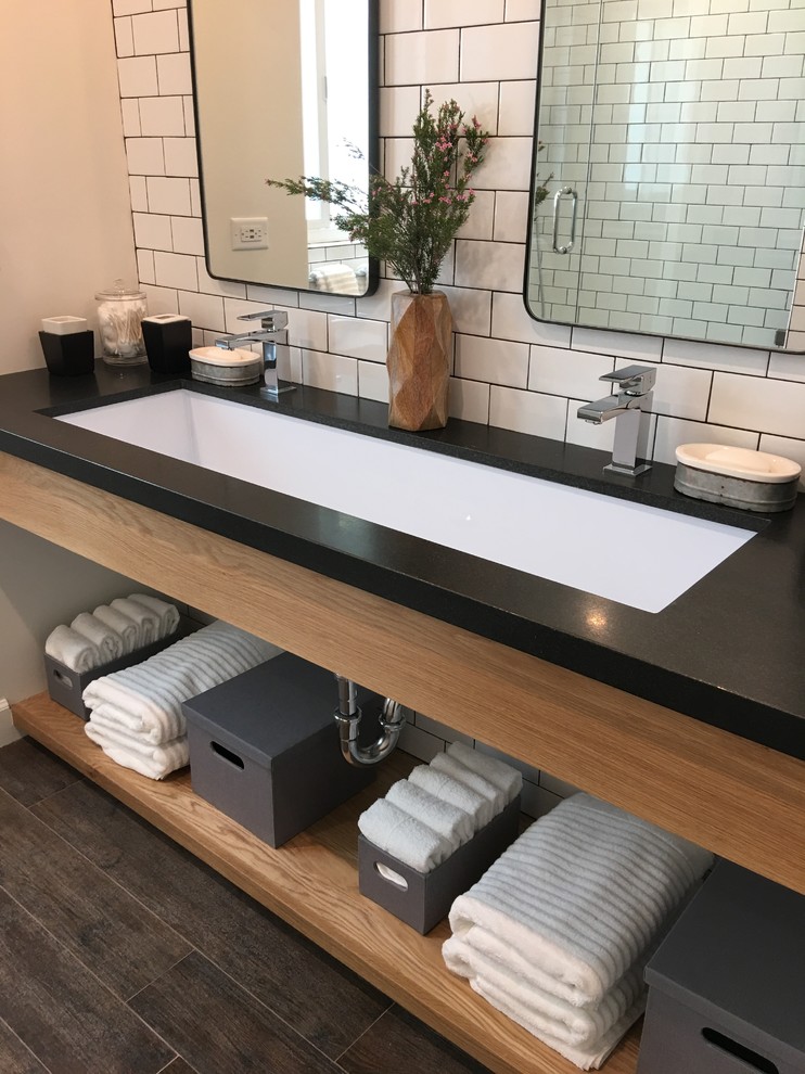 This is an example of a medium sized industrial bathroom in Los Angeles with open cabinets, medium wood cabinets, an alcove shower, a one-piece toilet, white tiles, metro tiles, white walls, ceramic flooring, a trough sink and granite worktops.