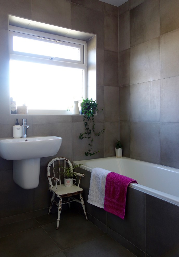 Photo of a small contemporary family bathroom in Other with glass-front cabinets, a built-in bath, a shower/bath combination, grey tiles, white walls, porcelain flooring and a wall-mounted sink.