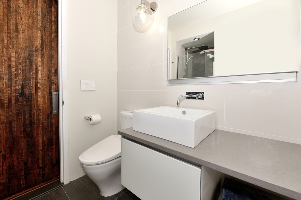 Example of a mid-sized trendy white tile and ceramic tile bathroom design in New York with a vessel sink, flat-panel cabinets, white cabinets, solid surface countertops, a one-piece toilet and white walls