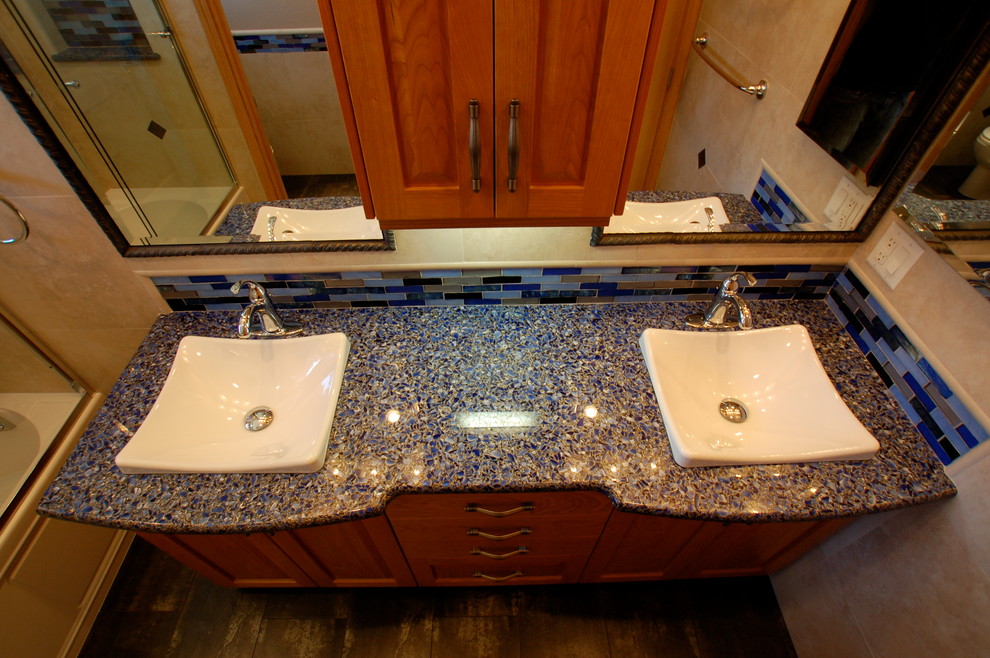 Cette image montre une salle d'eau bohème en bois brun de taille moyenne avec un placard à porte shaker, une baignoire en alcôve, un combiné douche/baignoire, WC à poser, un carrelage noir, un carrelage bleu, un carrelage gris, des carreaux en allumettes, un mur beige, un sol en carrelage de porcelaine, une vasque et un plan de toilette en verre recyclé.