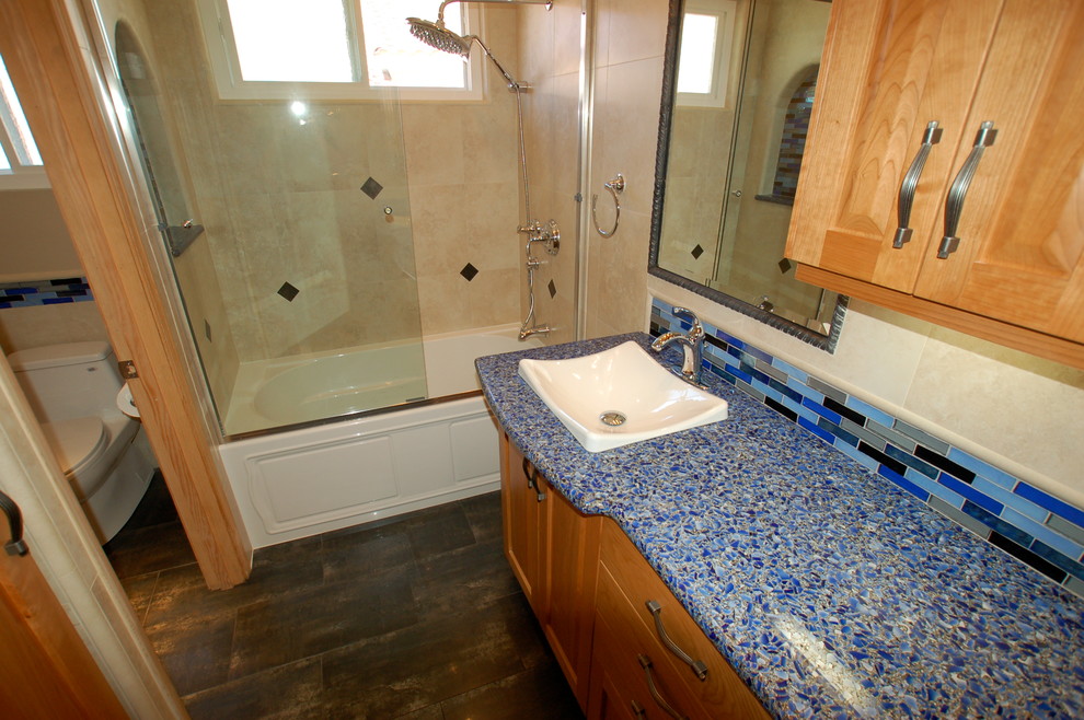 Inspiration för ett mellanstort eklektiskt badrum med dusch, med skåp i shakerstil, skåp i mellenmörkt trä, ett badkar i en alkov, en dusch/badkar-kombination, en toalettstol med hel cisternkåpa, svart kakel, blå kakel, grå kakel, stickkakel, beige väggar, klinkergolv i porslin, ett fristående handfat och bänkskiva i återvunnet glas