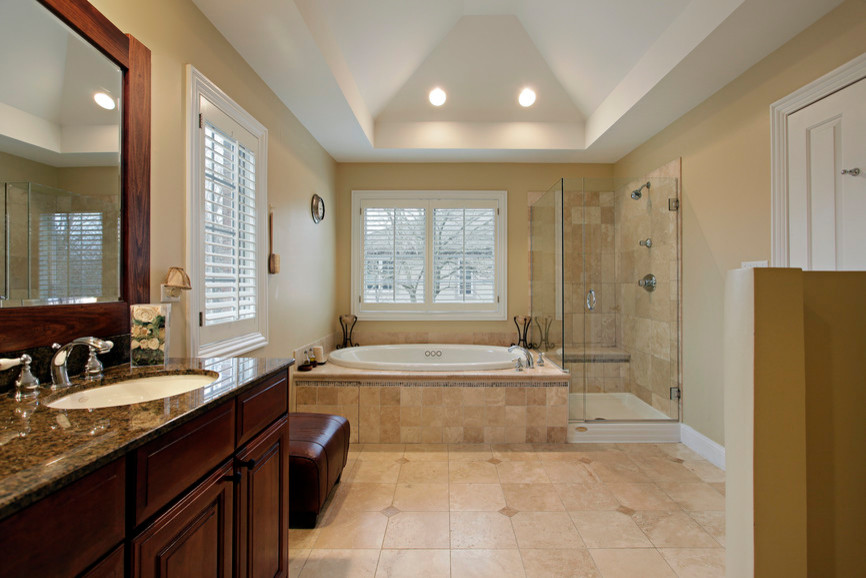 Large classic ensuite bathroom in New York with raised-panel cabinets, dark wood cabinets, a built-in bath, a corner shower, beige walls, porcelain flooring, a submerged sink, granite worktops, beige floors, a hinged door and multi-coloured worktops.