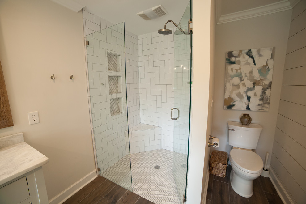 На фото: большая главная ванная комната в стиле модернизм с белыми фасадами, угловым душем, унитазом-моноблоком, белой плиткой, плиткой кабанчик, серыми стенами, темным паркетным полом, врезной раковиной, мраморной столешницей, коричневым полом и душем с распашными дверями