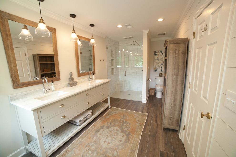 Photo of a large modern ensuite bathroom in Atlanta with freestanding cabinets, white cabinets, a corner shower, a one-piece toilet, white tiles, metro tiles, grey walls, dark hardwood flooring, a submerged sink, marble worktops, brown floors and a hinged door.