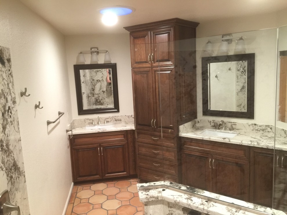Large rustic ensuite bathroom in Phoenix with raised-panel cabinets, brown cabinets, a corner shower, a two-piece toilet, black and white tiles, stone slabs, white walls, terracotta flooring, a built-in sink, granite worktops, brown floors, an open shower and white worktops.
