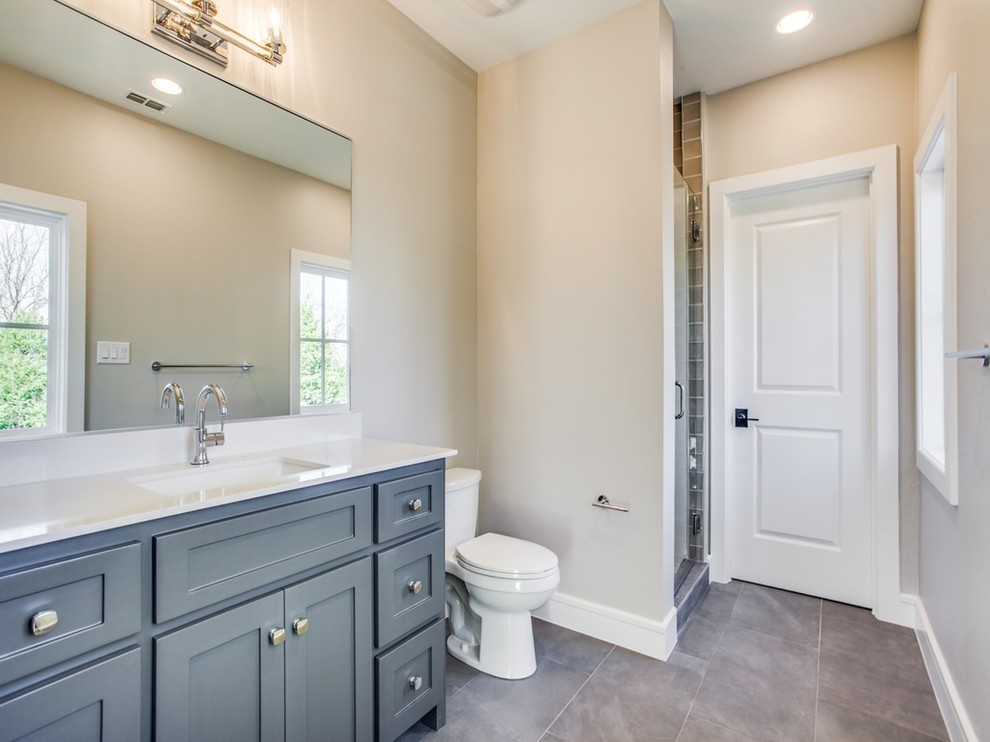 Alcove shower - mid-sized traditional 3/4 brown tile porcelain tile and gray floor alcove shower idea in Other with shaker cabinets, gray cabinets, a two-piece toilet, beige walls, an undermount sink, solid surface countertops, a hinged shower door and white countertops