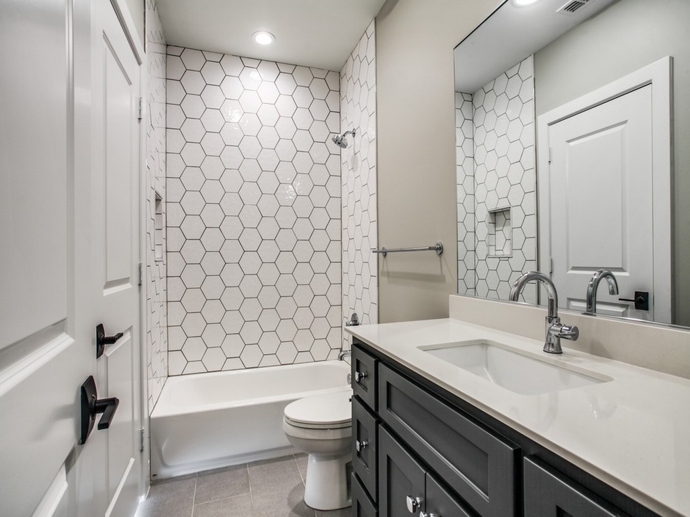 Cette photo montre une salle d'eau chic de taille moyenne avec un placard à porte shaker, des portes de placard grises, une baignoire en alcôve, un combiné douche/baignoire, un carrelage blanc, des carreaux de porcelaine, un mur beige, un sol en carrelage de porcelaine, un lavabo encastré, un plan de toilette en surface solide, un sol gris et un plan de toilette blanc.