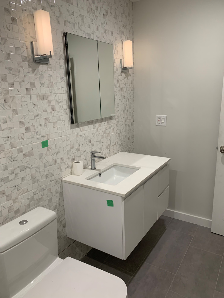 Medium sized modern ensuite bathroom in New York with flat-panel cabinets, white cabinets, a walk-in shower, a one-piece toilet, white tiles, porcelain tiles, grey walls, porcelain flooring, a submerged sink, engineered stone worktops, grey floors, a hinged door, white worktops, a wall niche, a single sink and a floating vanity unit.