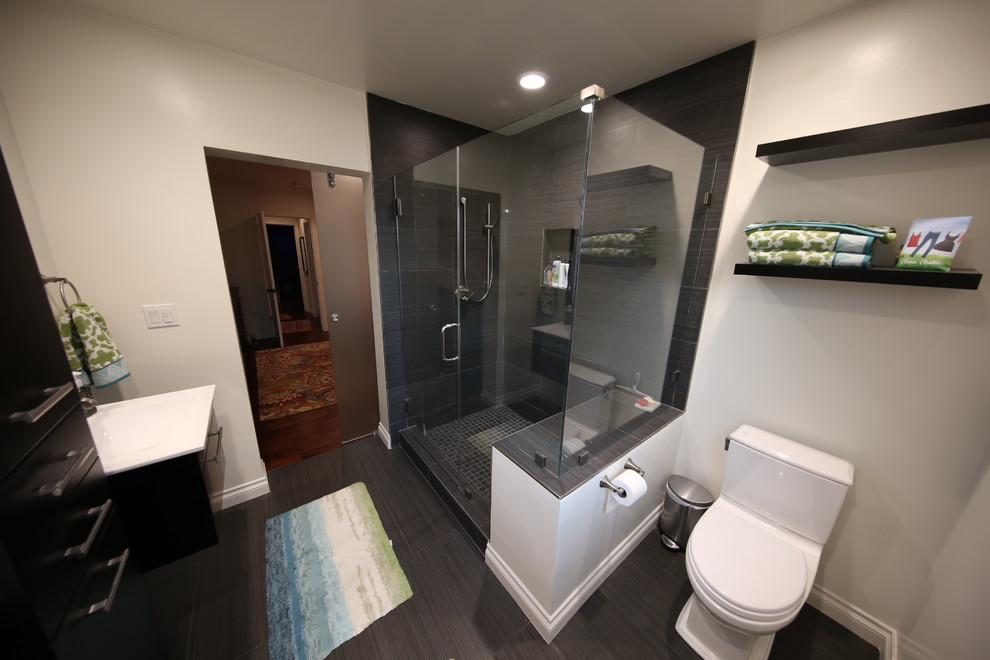 Стильный дизайн: главная ванная комната среднего размера в современном стиле с плоскими фасадами, черными фасадами, угловым душем, белыми стенами, монолитной раковиной, унитазом-моноблоком, черной плиткой, керамогранитной плиткой, полом из керамогранита, столешницей из искусственного камня, серым полом, душем с распашными дверями, белой столешницей, тумбой под две раковины и подвесной тумбой - последний тренд