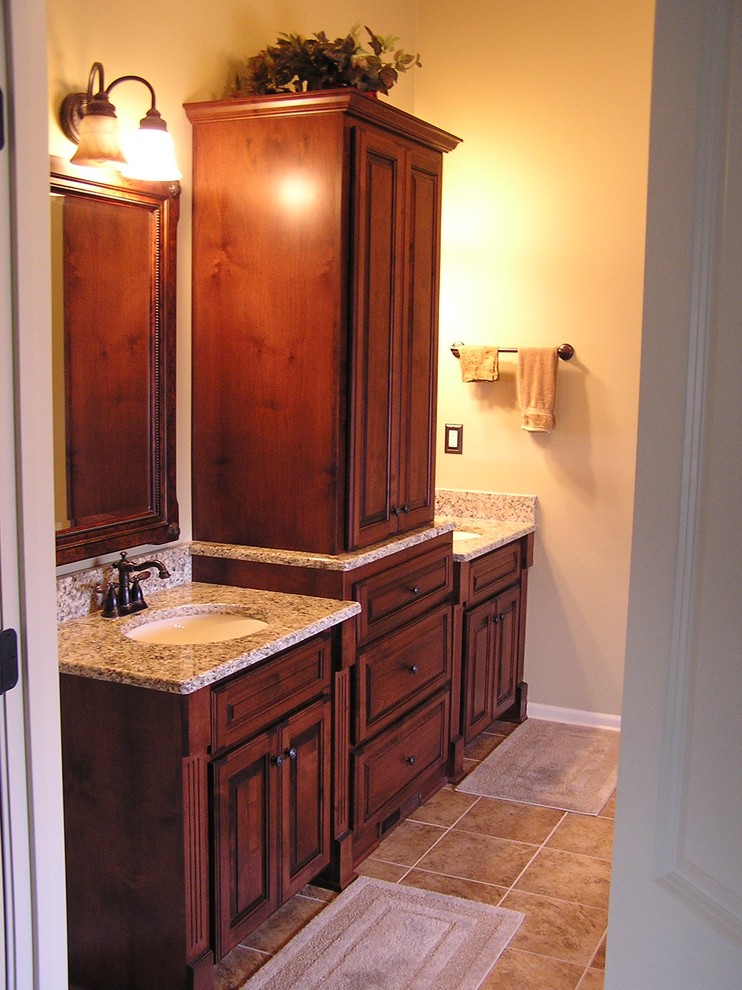 Cette image montre une salle de bain principale traditionnelle en bois foncé de taille moyenne avec un placard avec porte à panneau surélevé, un mur beige, un sol en carrelage de porcelaine, un lavabo encastré, un plan de toilette en granite et un sol beige.