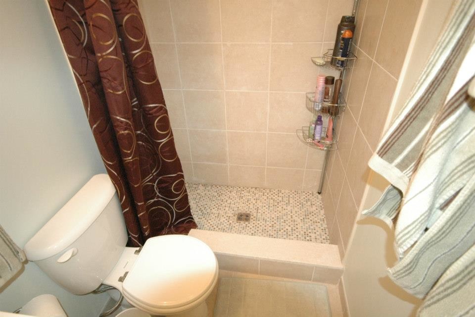 Kleines Badezimmer mit Mineralwerkstoff-Waschtisch, Duschbadewanne, Toilette mit Aufsatzspülkasten, beigen Fliesen, weißer Wandfarbe und Keramikboden in Baltimore