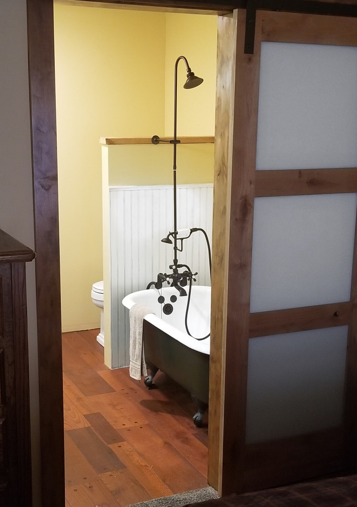 Immagine di una stanza da bagno padronale stile rurale di medie dimensioni con mobile bagno freestanding, consolle stile comò, ante in legno scuro, vasca con piedi a zampa di leone, vasca/doccia, WC a due pezzi, pareti gialle, pavimento in legno massello medio, lavabo da incasso, top in legno, pavimento marrone, doccia con tenda, top marrone, due lavabi e pannellatura