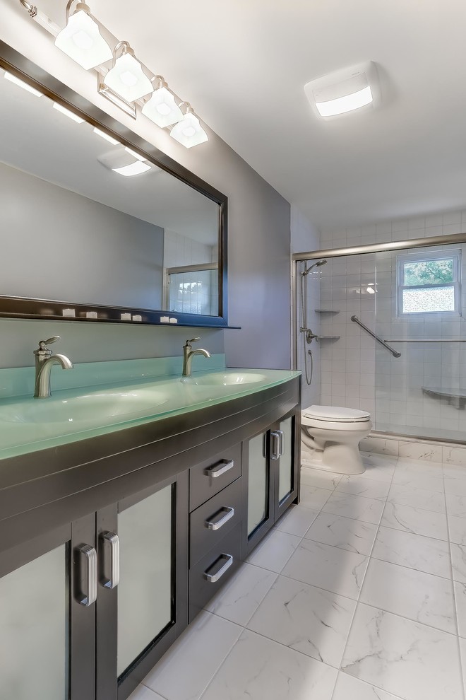 Cette photo montre une salle de bain chic en bois foncé de taille moyenne avec un placard à porte vitrée, WC à poser, un mur gris, un sol en marbre, un lavabo intégré et un plan de toilette en verre.