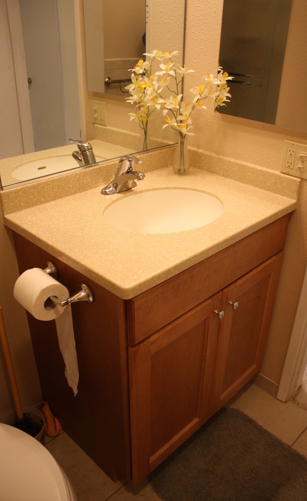This is an example of a small classic family bathroom in San Diego with an integrated sink, recessed-panel cabinets, medium wood cabinets, solid surface worktops, an alcove bath, a shower/bath combination, a two-piece toilet, beige tiles, porcelain tiles, beige walls and porcelain flooring.