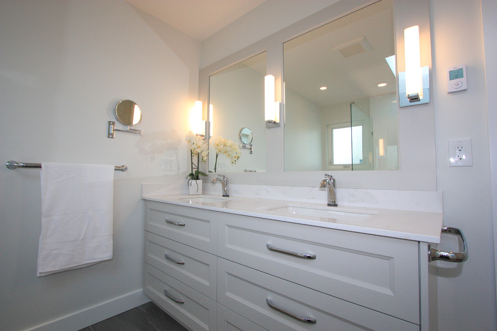 Photo of a traditional ensuite bathroom in Vancouver with a submerged sink, recessed-panel cabinets, white cabinets, solid surface worktops, a corner shower, a two-piece toilet, white tiles, ceramic tiles and white walls.