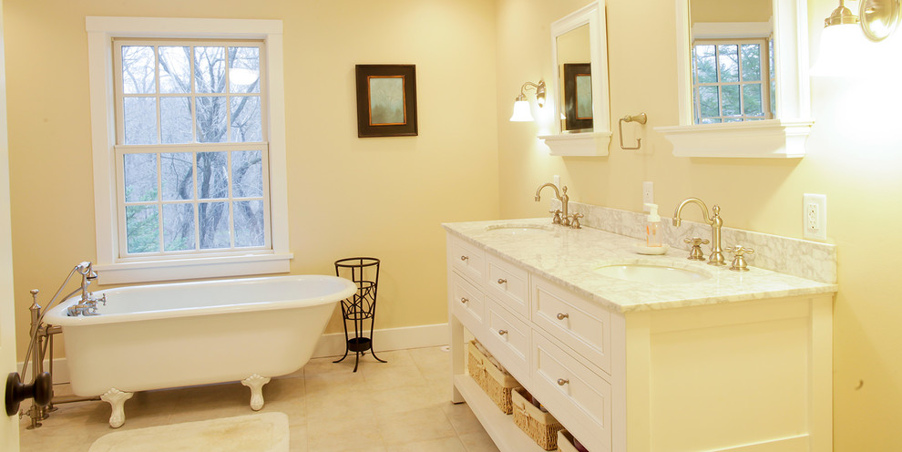 Cette photo montre une salle de bain principale chic avec un placard à porte shaker, des portes de placard blanches, une baignoire sur pieds, un mur jaune, un sol en carrelage de céramique et un lavabo encastré.