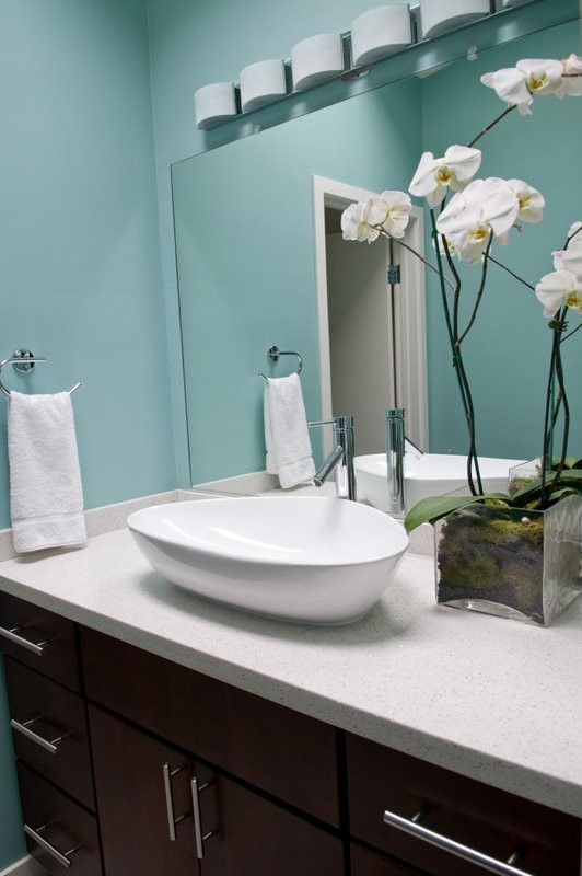 Cette image montre une salle de bain design en bois foncé avec un placard à porte plane, WC séparés, un carrelage beige, un carrelage gris, une plaque de galets, un mur bleu, un sol en galet, une vasque et un plan de toilette en quartz.
