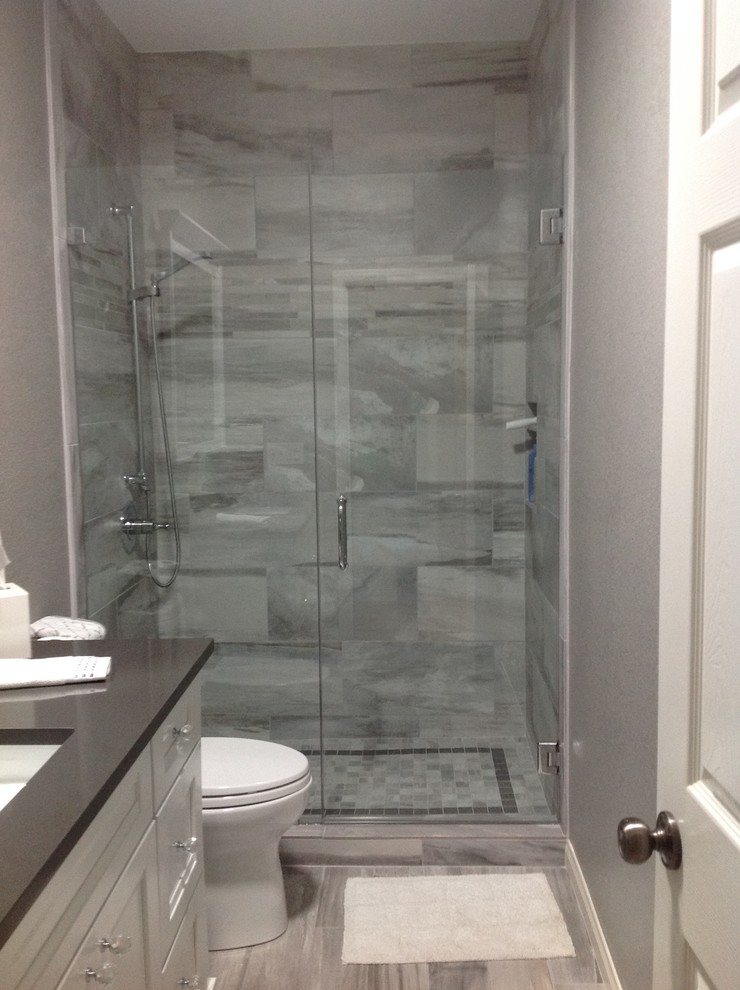 Inredning av ett klassiskt mellanstort badrum med dusch, med luckor med infälld panel, vita skåp, en dusch i en alkov, en toalettstol med hel cisternkåpa, grå kakel, vit kakel, porslinskakel, grå väggar, klinkergolv i porslin, ett undermonterad handfat och bänkskiva i akrylsten