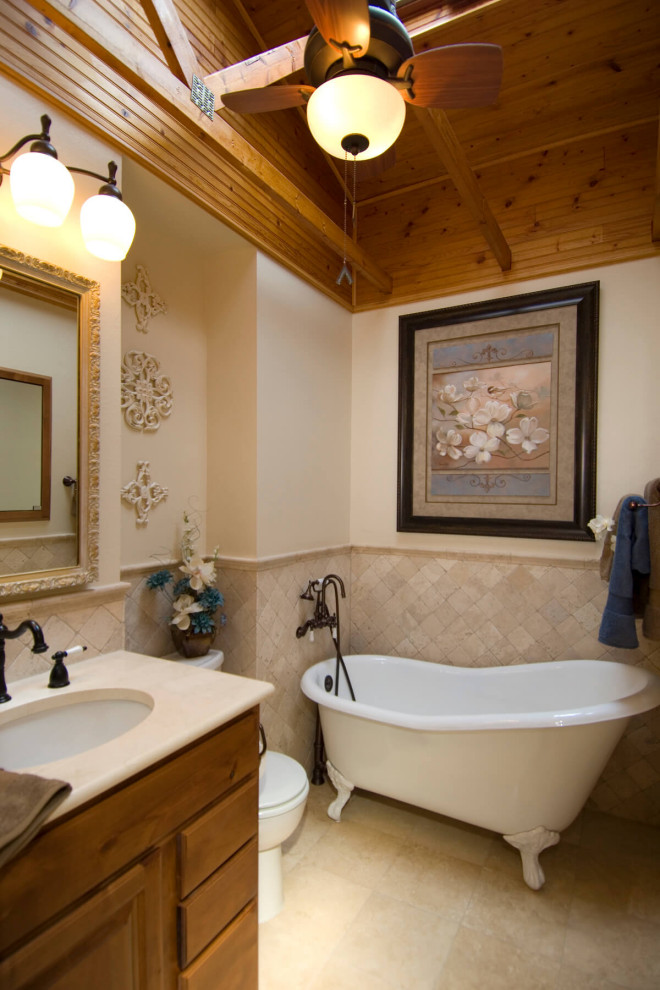 Exemple d'une salle de bain principale en bois brun de taille moyenne avec un placard à porte plane, une baignoire sur pieds, un carrelage beige, du carrelage en travertin, un mur beige, un sol en travertin, un lavabo encastré, un plan de toilette en marbre, un sol beige, aucune cabine, un plan de toilette beige, meuble simple vasque, meuble-lavabo sur pied, un plafond voûté et boiseries.