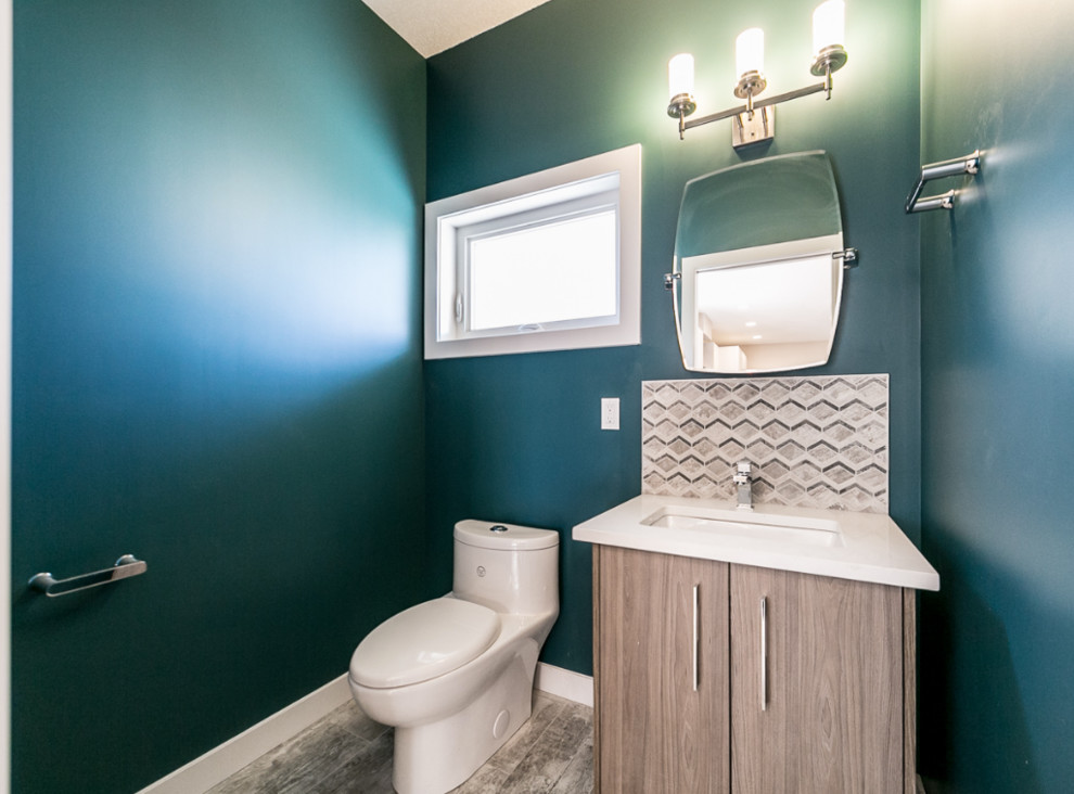 Klassisk inredning av ett litet badrum med dusch, med släta luckor, skåp i mellenmörkt trä, en toalettstol med hel cisternkåpa, blå väggar, vinylgolv, ett undermonterad handfat och bänkskiva i akrylsten
